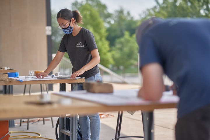 Two people working at worktables on a patio.