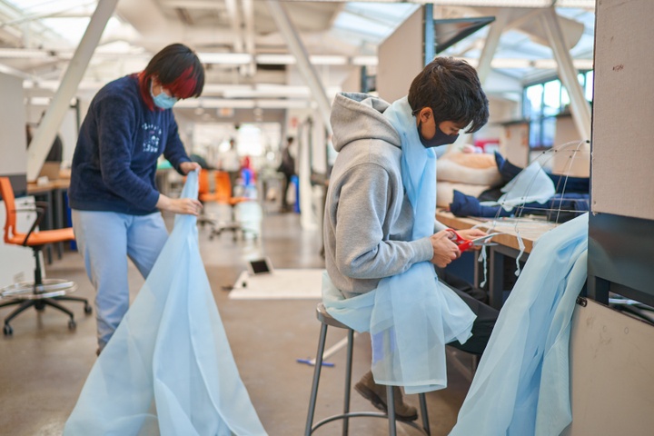 Two people work with a long strip of pale blue chiffon in a brightly-lit studio space.