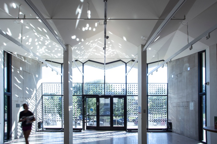 Open lobby area of Steinberg Hall, with reflections of light on the walls and ceilings, cast by a series of small mirrored surfaces hung along the floor-to-ceiling glass windows and doors on the back wall.