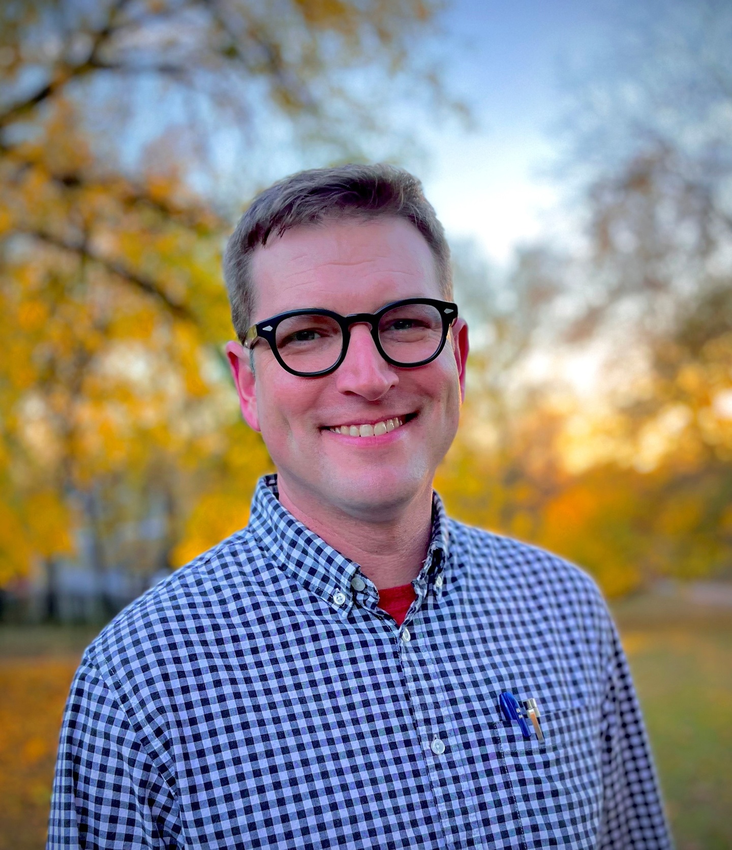 headshot of John Hendrix, wearing blue and glasses with fall leaves in the background