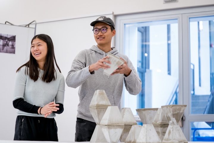 Two smiling students present a construction of modular, polygonal concrete pieces.
