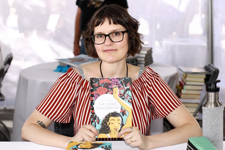 Photo of Eleanor Davis seating, holding her book titled *The Hard Tomorrow*