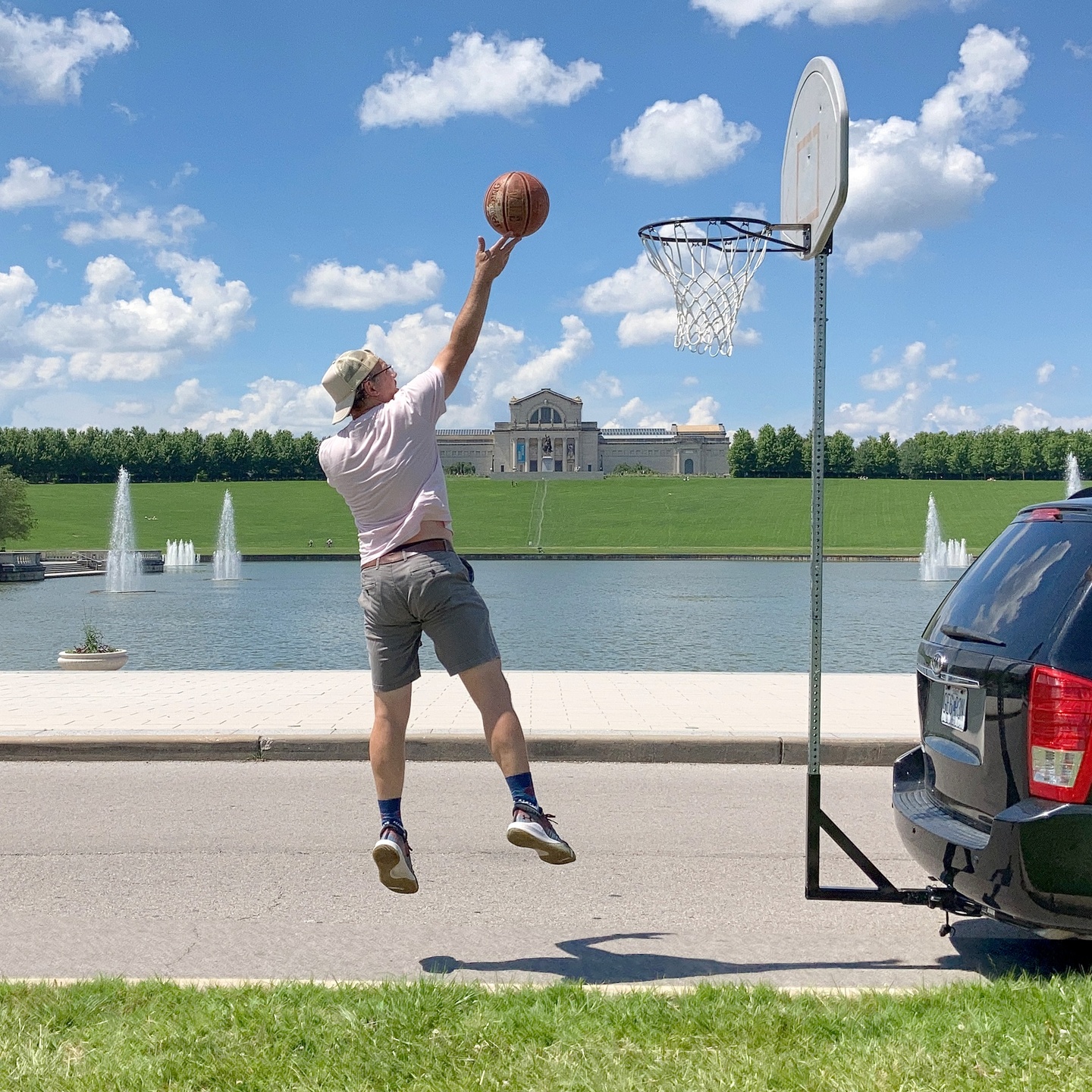 An individual jumping and shooting a basketball, on a temporary court in front of St. Louis Forest Park's Grand Basin