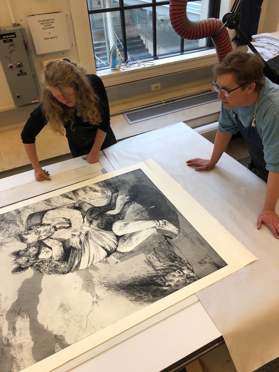 Artist and printer lean over a fresh print to inspect it just after printing.