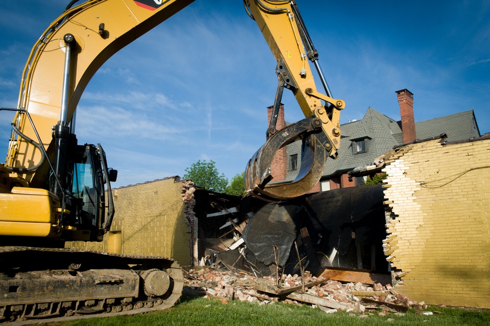 Heavy machinery destroys a wall that is painted gold. 