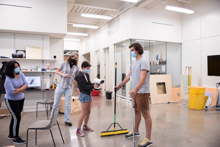 Person poses with arms spread while another aims a handheld scanning device at them.