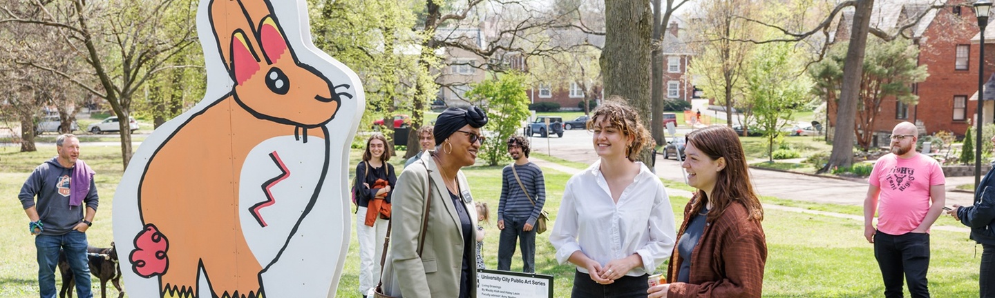 People in a park talking with a sculpture of a bunny behind them.