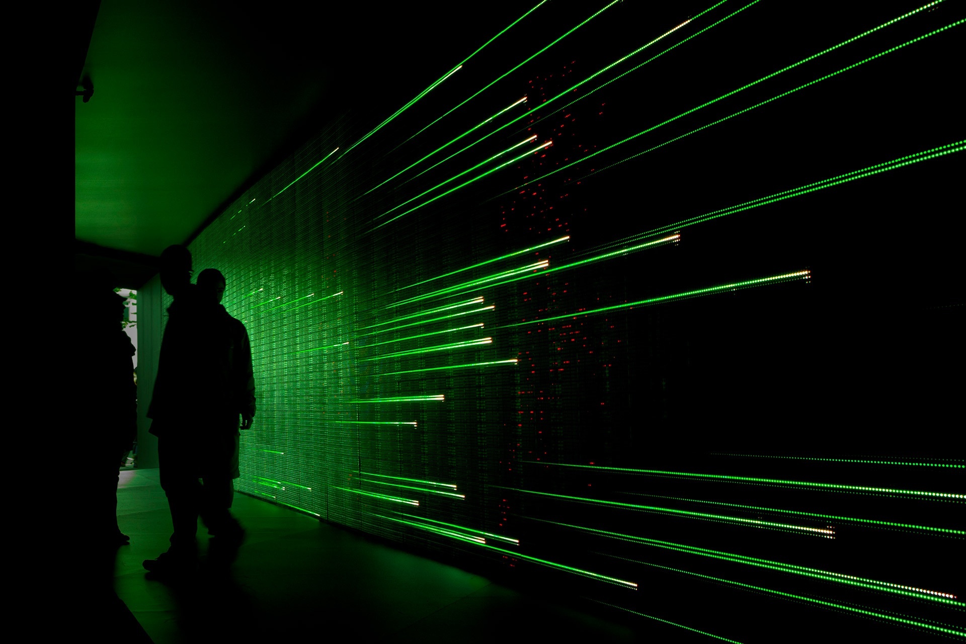 People in a dark space in front of digital surface that has thin green lines running across it.