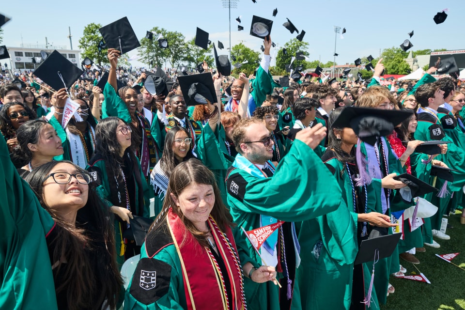 Students wearing regalia throw their graduation caps into the air and cheer for each other