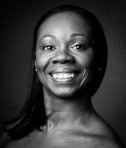 A black-and-white headshot of dancer and RRDC artistic director Kim Grier-Martinez. She is a Black woman whose hairs falls gracefully on her bare shoulder. She smiles, beaming at the camera.