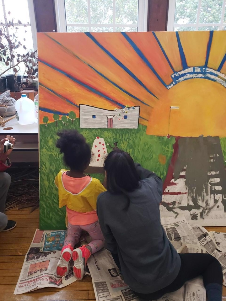 Student paints mural indoors with a child.