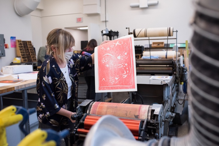 Person lifts a red print off of a roller press.