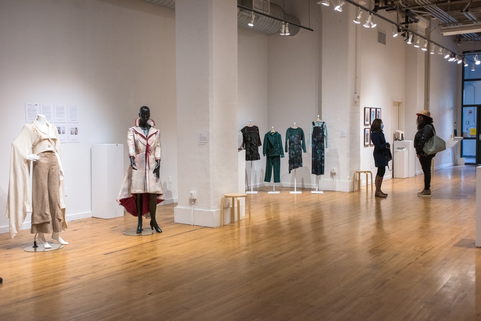 A gallery space with two people in it and two displays of fashion design collections.