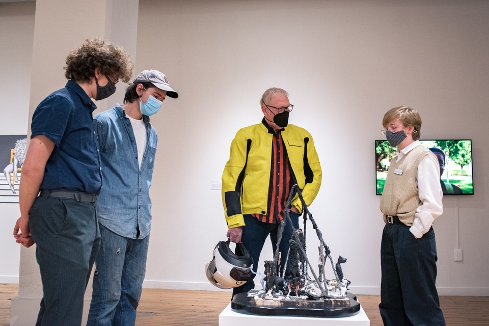 Four people stand around a black viney sculpture on a low plinth and discuss.