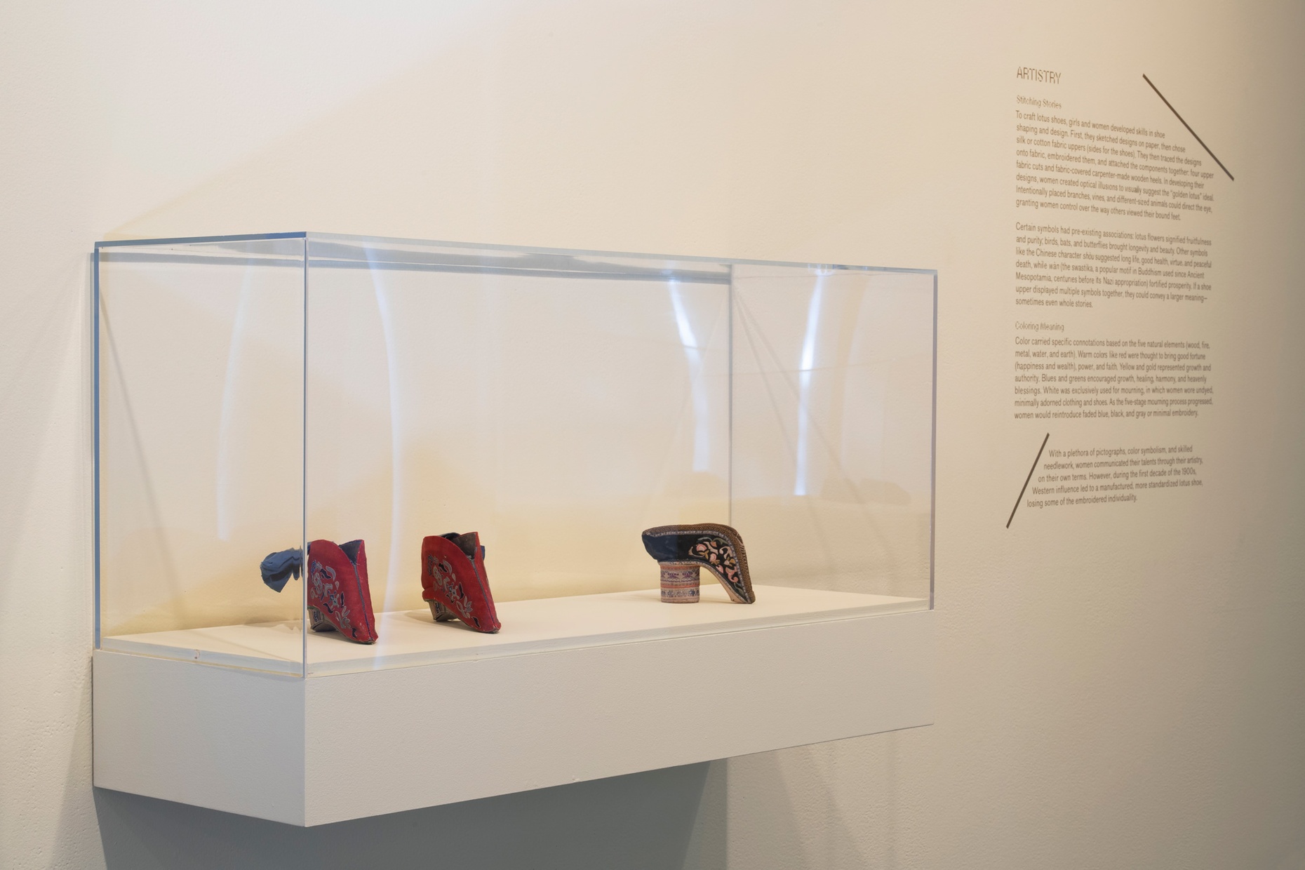 A glass case holding three small embroidered shoes.