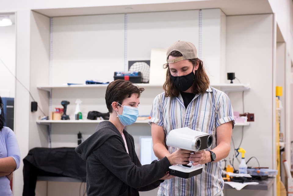 Instructor shows a student how to operate a handheld 3D scanning device.