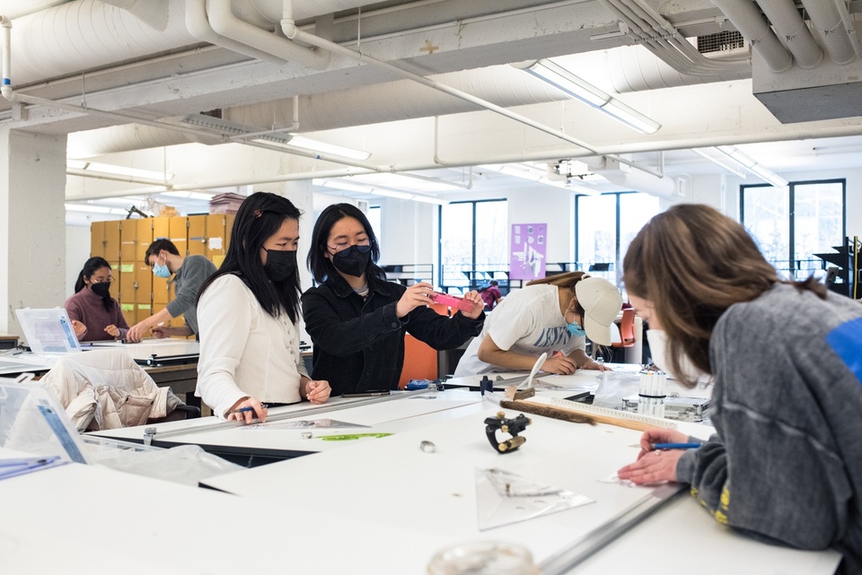 Group of people in a studio space working on various drafting boards and talking.