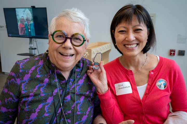 Georgia and friend hold up a sticker that is a cartoon of Georgia wearing a tall, white, curly wig.