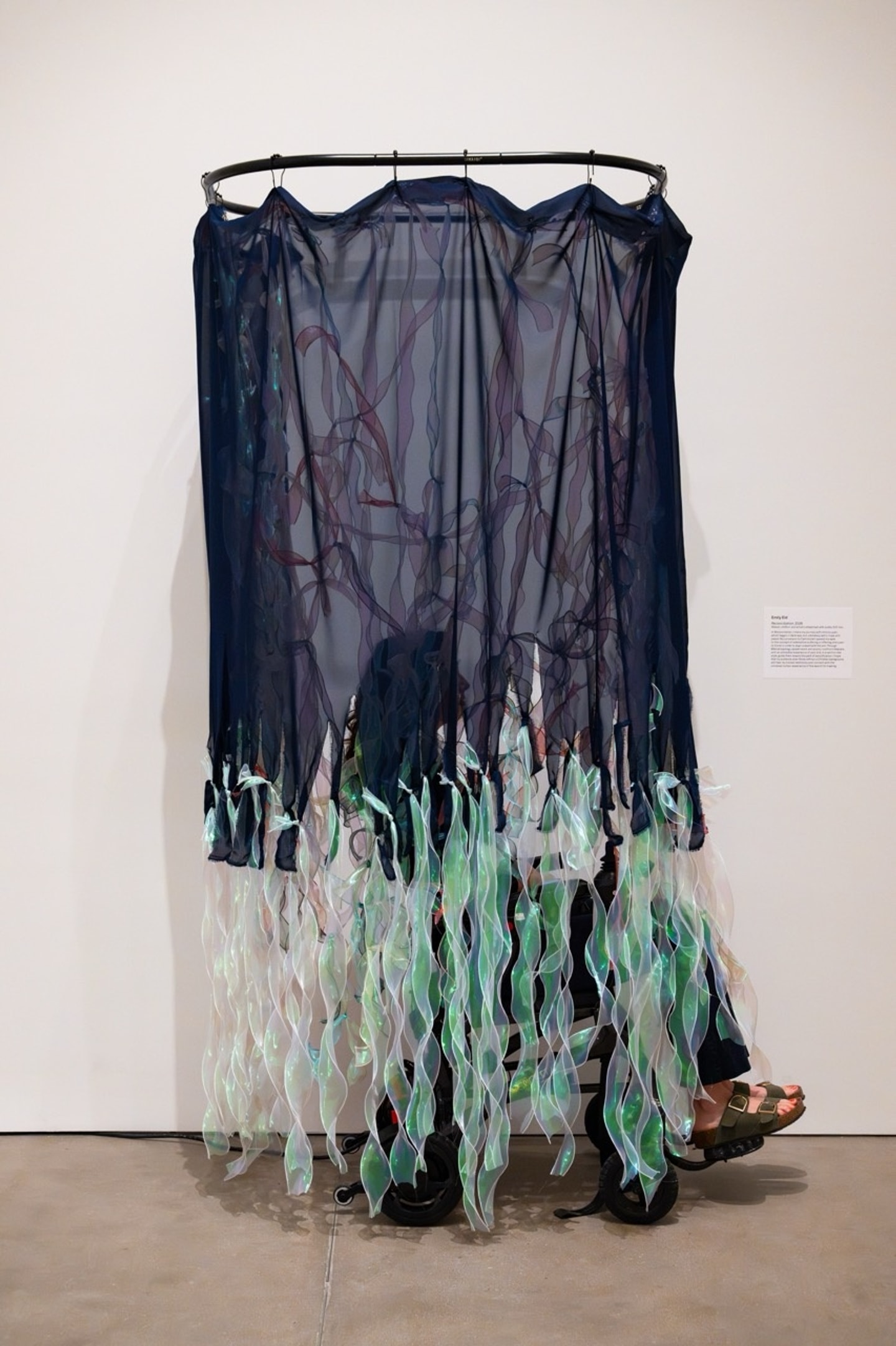 a wheelchair surrounded by a curtain made of chiffon and ribbon in a gallery