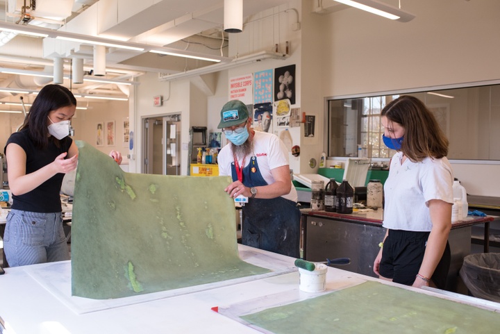 Two people pull a cyanotype print off a worktable in a printmaking studio space.