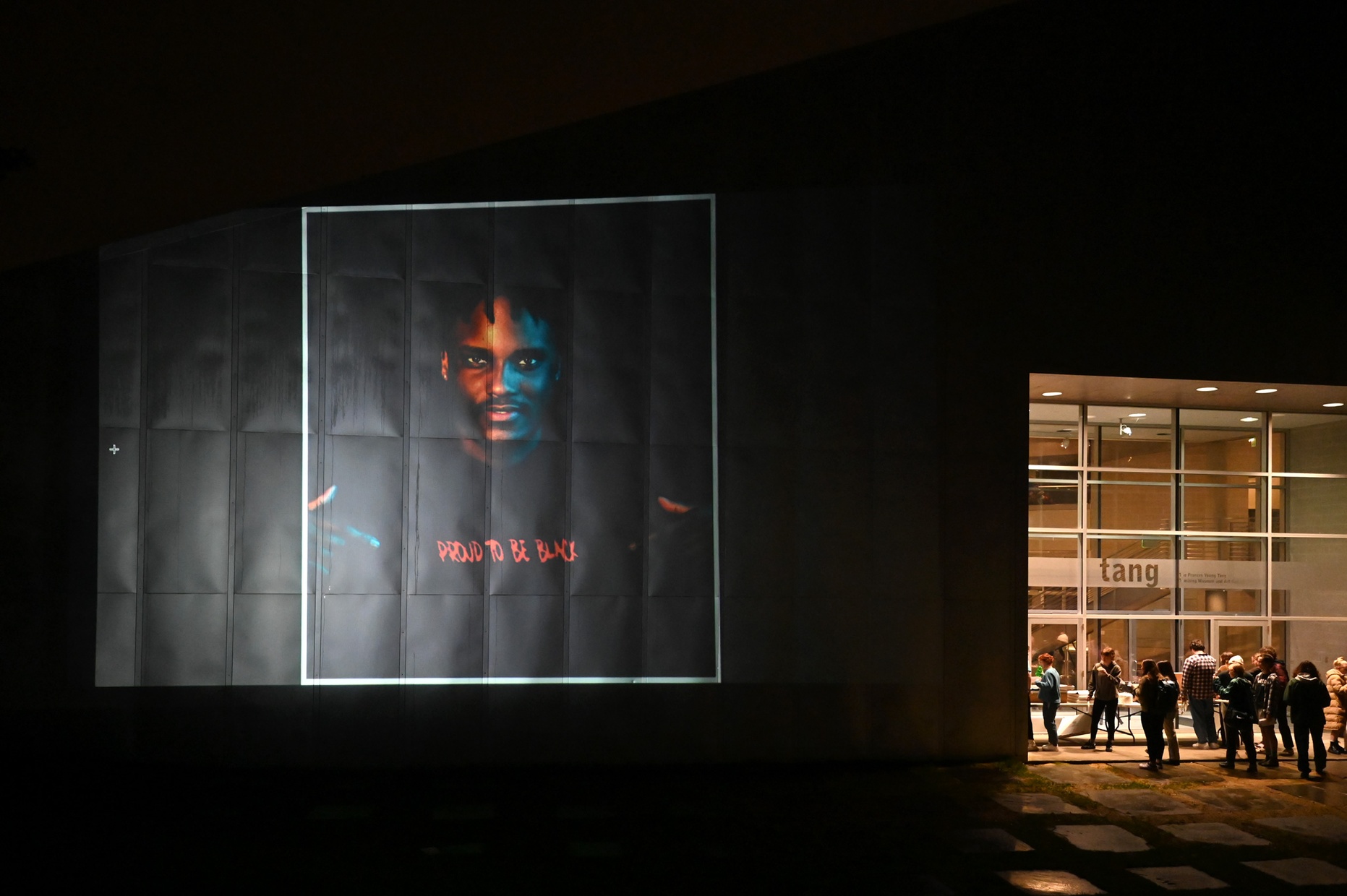 A projection against the side of a building shows a Black man with a shirt that reads "PROUD TO BE BLACK."