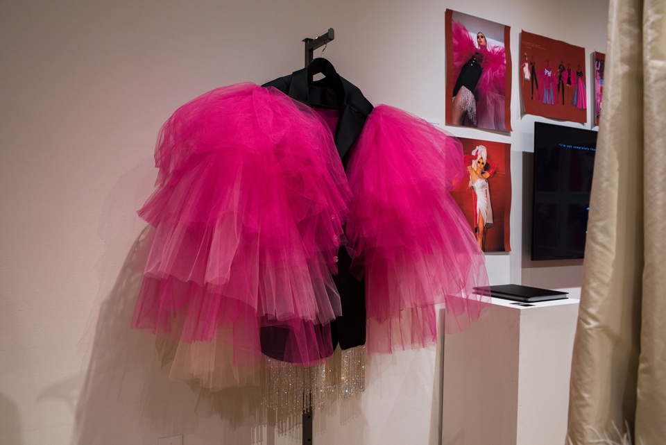 Black blazer on a hanger with huge magenta ruffs of tulle over the sleeves.