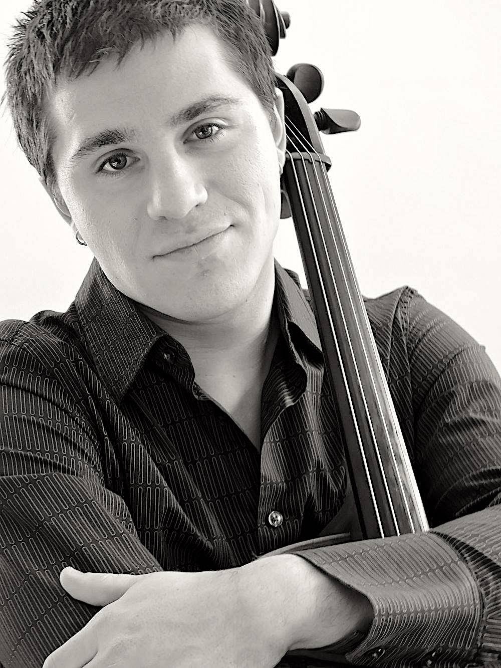 A musician wearing a button down shirt with one arm crossed across his chest holding the neck of a cello up against his shoulder and behind his head.