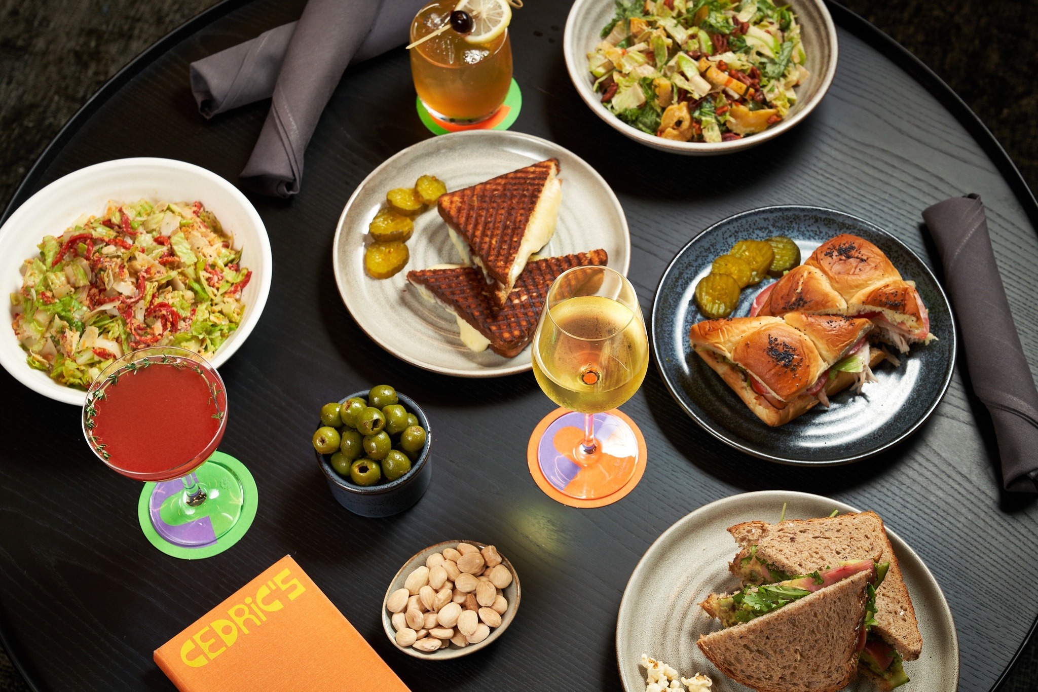 Image of a black table with assorted plates of sandwiches, salads, and cocktails.