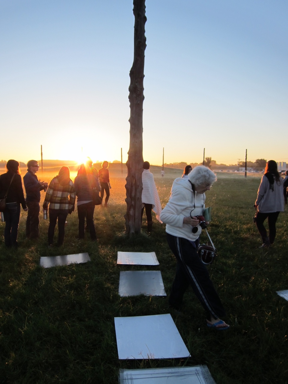 A group of people outdoors on a field in the evening with rectangular silver sheets arranged  on the ground