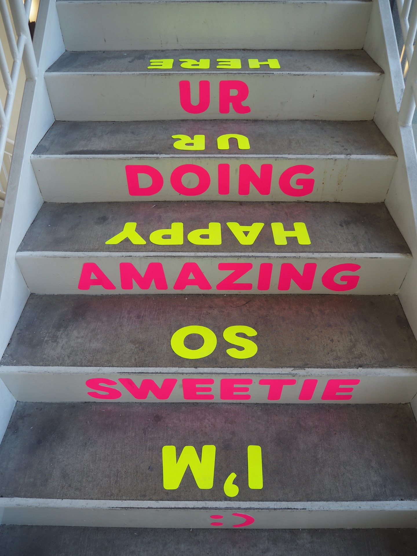Photo of concrete stairs: risers neon pink text read UR DOING AMAZING SWEETIE :) , treads neon yellow text read I'M SO HAPPY UR HERE.