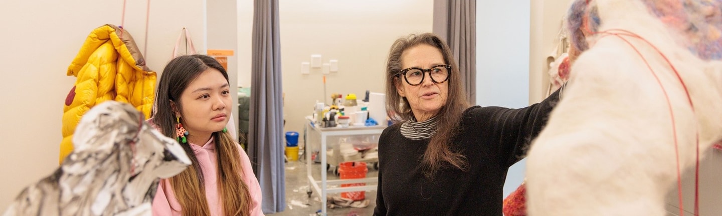 A student and her professor discuss the student's sculpture in her studio space
