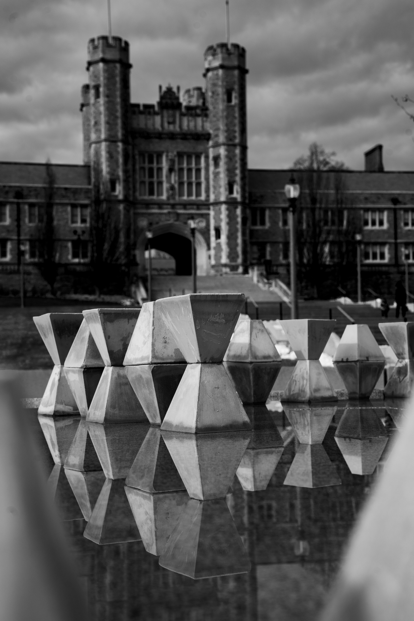 Assembly of modular concrete pyramids with flat tops stacked 2 high on a reflective surface outside. Behind them can be seen Brookings Hall on Washington University's campus.