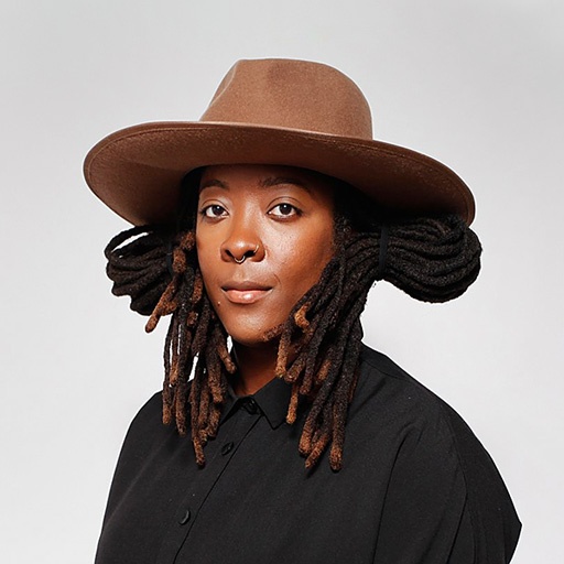 A Black woman with her hair cradling her head under a wide-brimmed brown hat. 