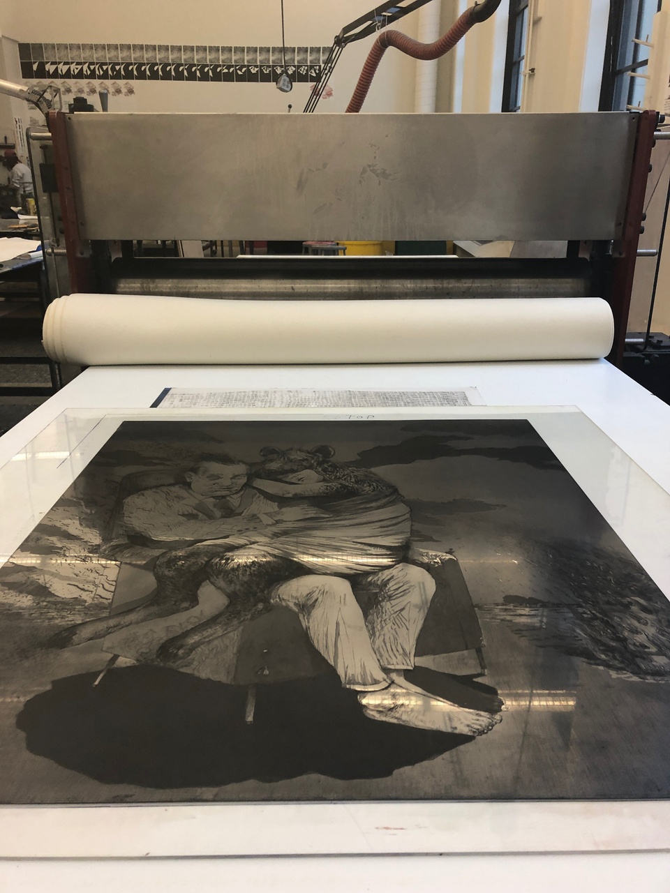 Large inked etching plate on bed of printing press.