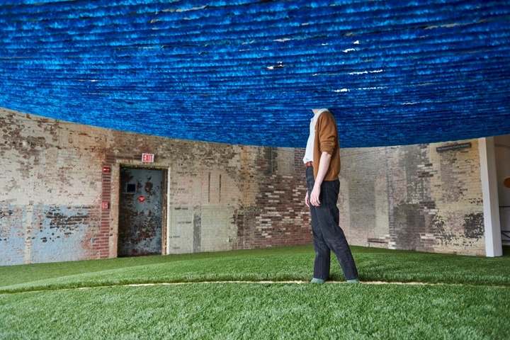 Terra installation view. A person walks through the installation, their head disappearing into the blue yarn cloud above it.