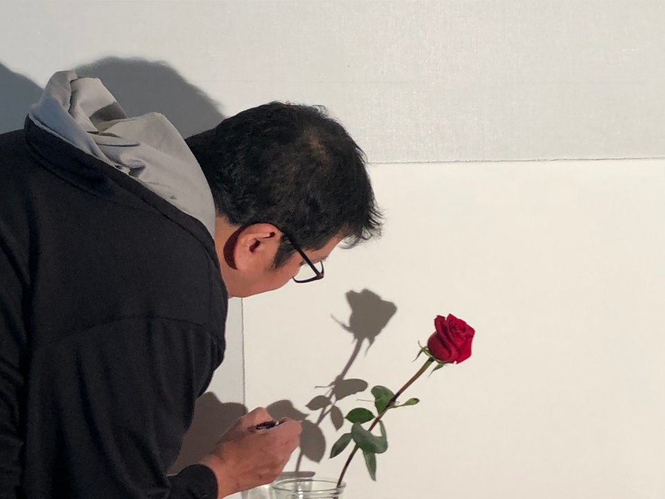 Artist tracing shadow of red rose on wall