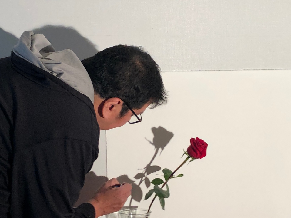 Artist tracing shadow of red rose on wall
