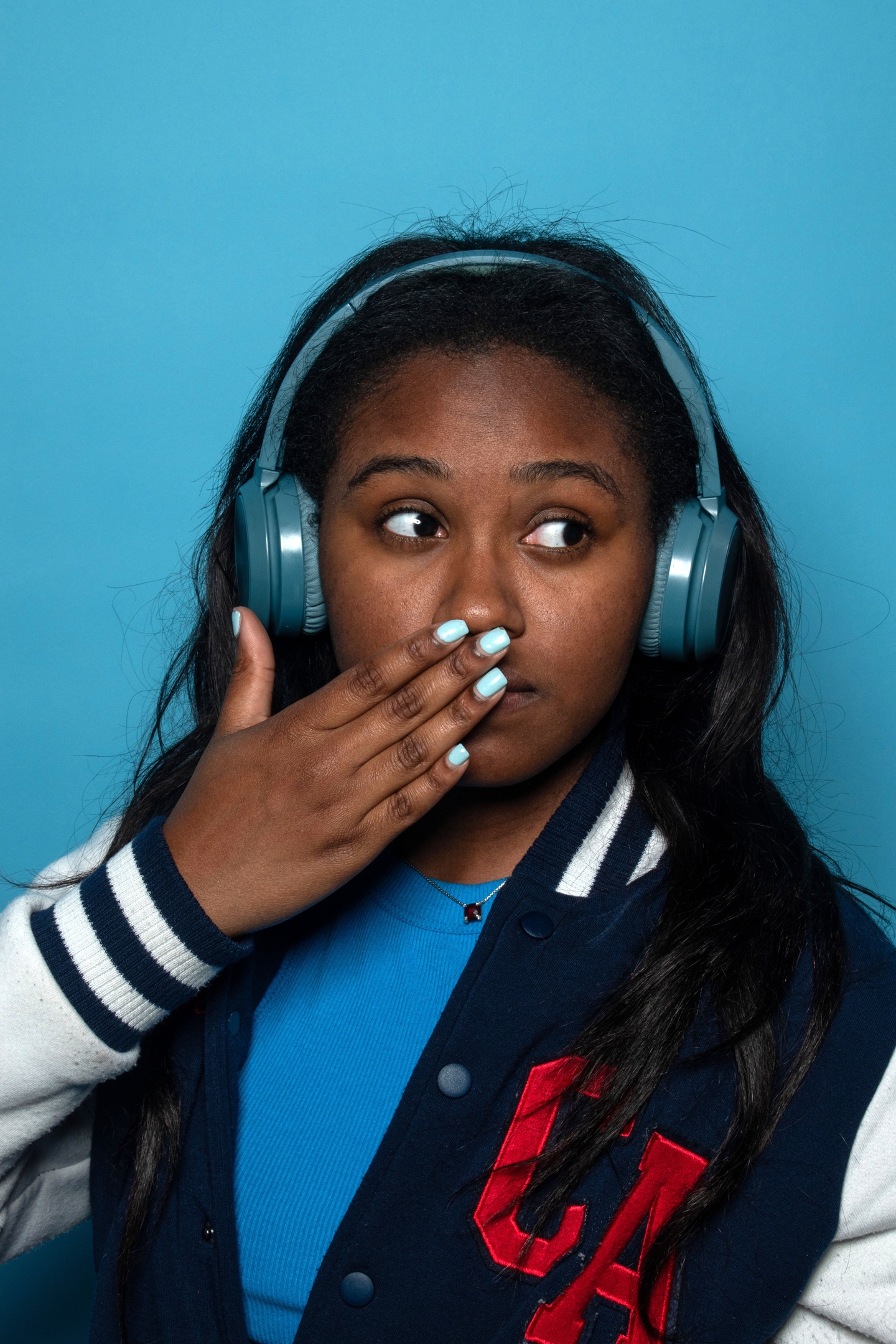 A photograph of a girl with her hand to her mouth in front of a blue background.