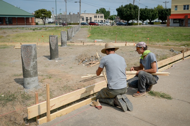 Two people kneel in front of a wood board in a field, assembling items together. 