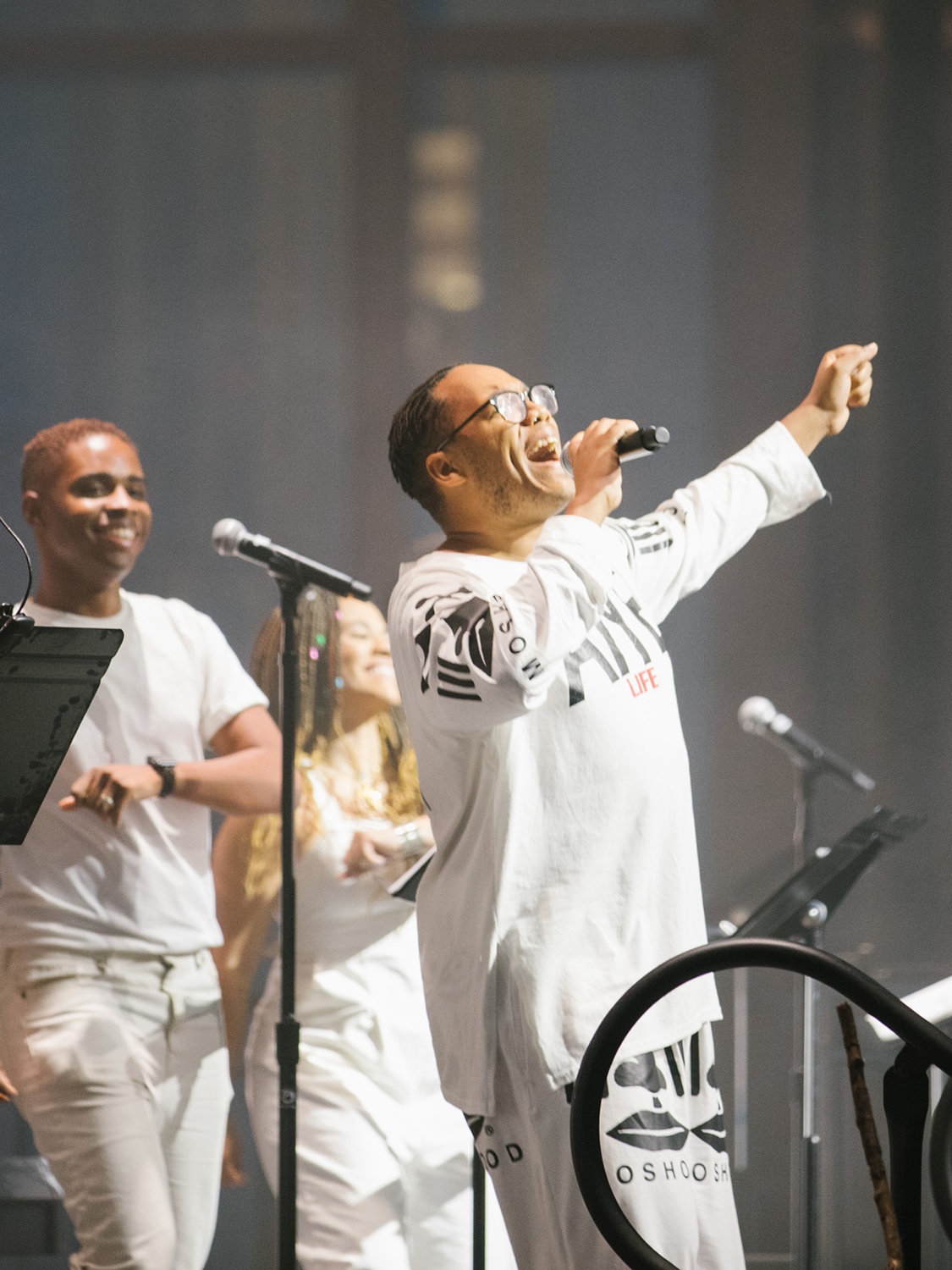 The artist Troy Anthony singing with arms outstretched in front of other performers. They all wear white costumes. 