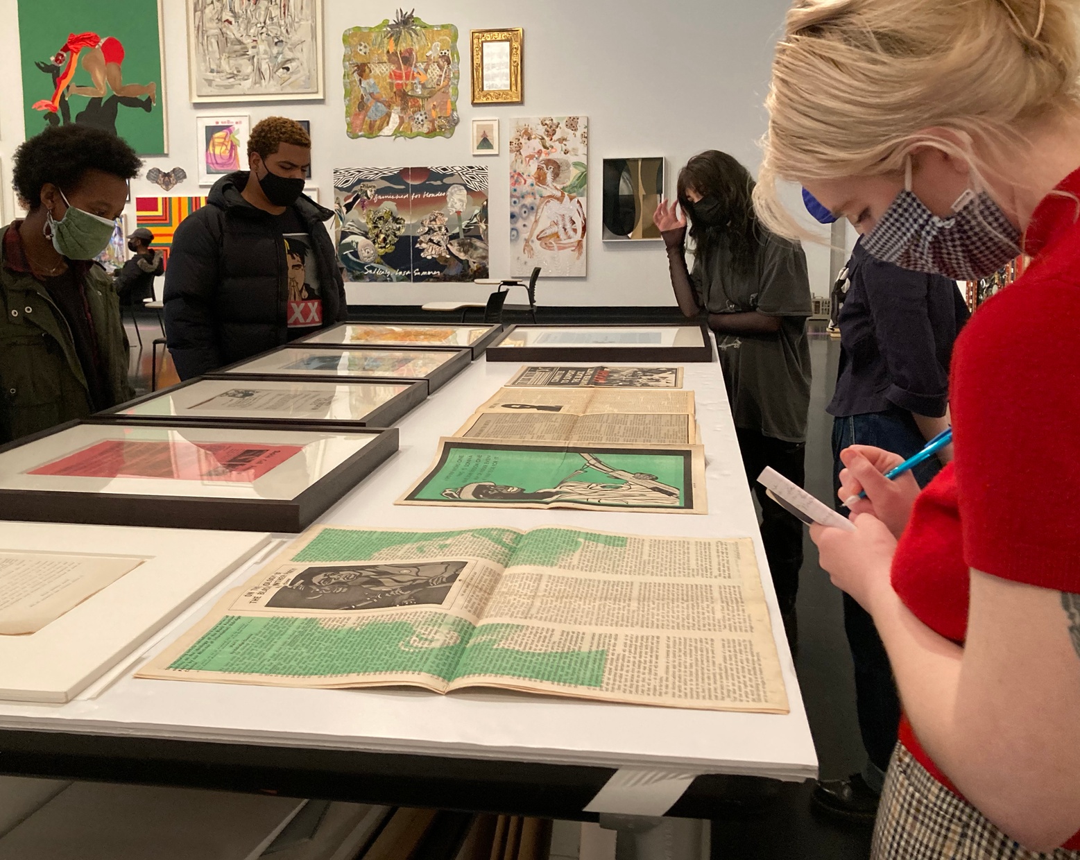 College students surrounding a table of framed and unframed materials taking notes.
