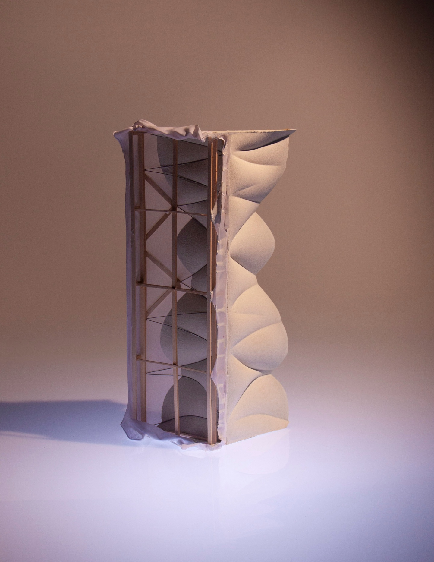 Plaster cast column with a wavy profile and indentations, photographed next to a wooden frame constructed with wire and covered in fabric that appears to be the basis for the plaster mold.
