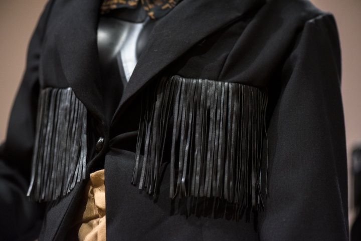 Detail view of a black blazer with black leather fringe sewn across the breast.