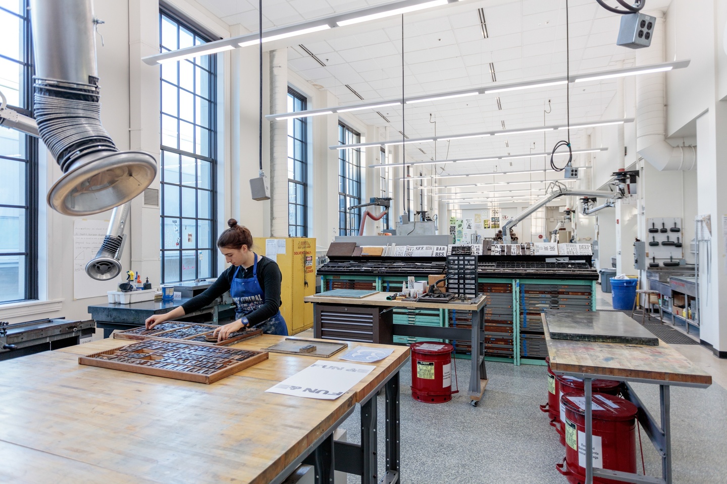 Person arranges a tray of moveable type on a table in a printmaking space with high ceilings.