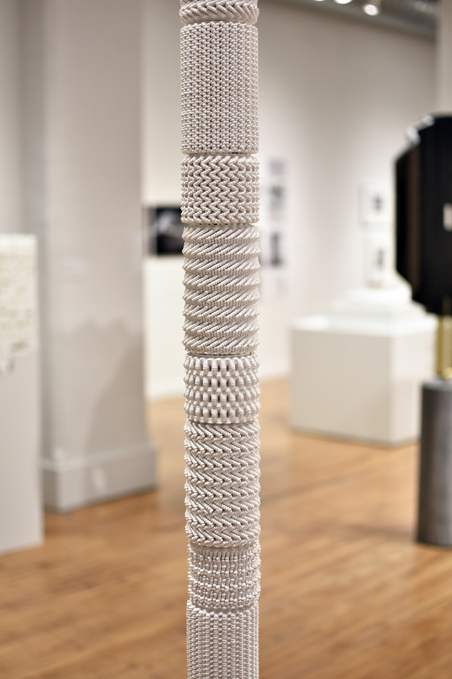 Digitally designed white totem comprised of eighteen aggregated cylinders, based on the same sine curve radiated around a circle.