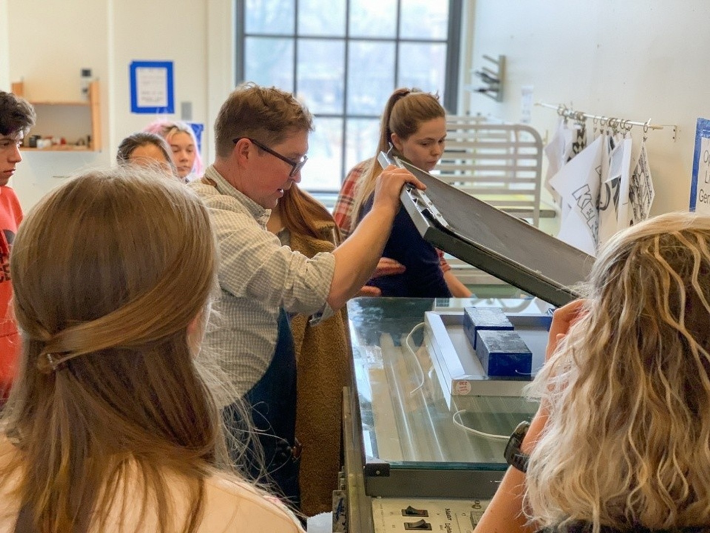 Teacher demonstrating silk screening while students stand and learn