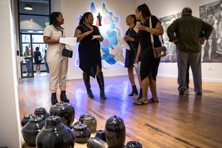 Gallery visitors in front of Jamie Harris' black ceramic urns on sand on the gallery floor