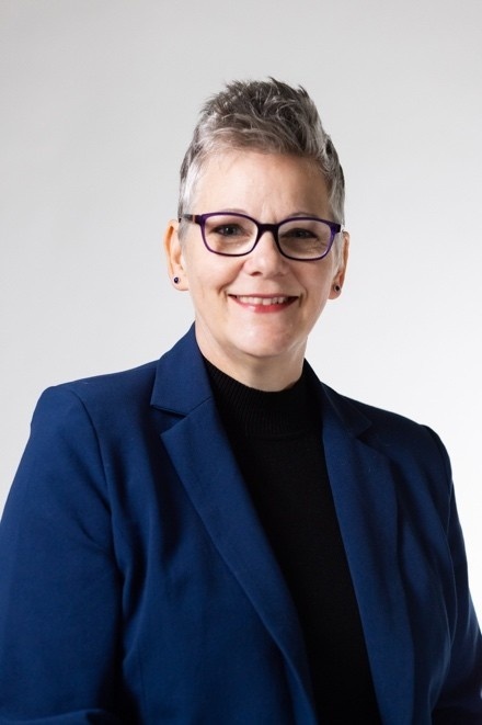 Jill Downen with short gray hair and glasses wearing a dark blue blazer