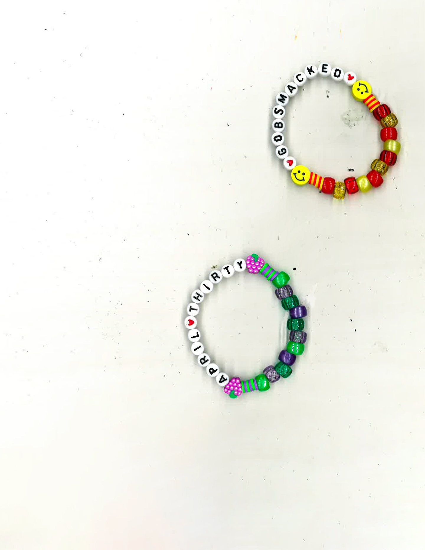 A pair of beaded bracelets on a white background; the top one includes the word Gobsmacked and the bottom one includes the words April Thirty.