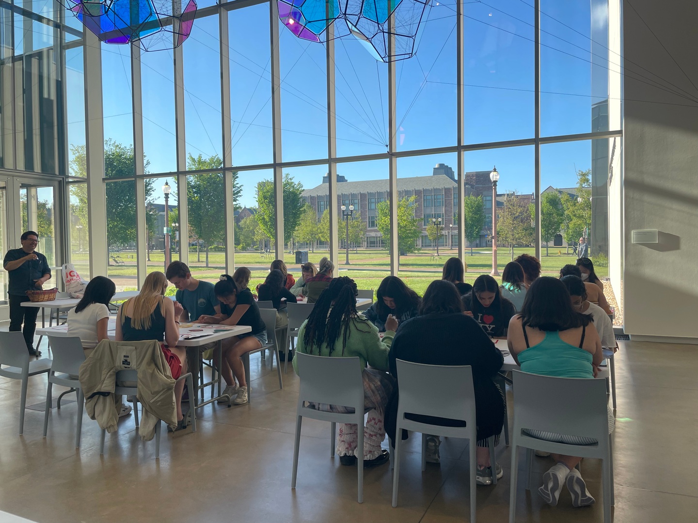 People sitting at tables in front of tall windows, working on art projects